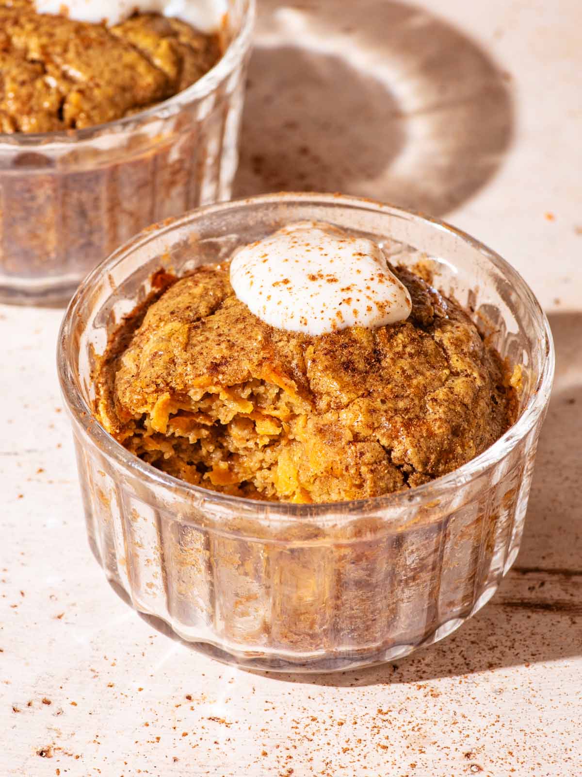 Baked oats in small glass ramekins, topped with yogurt, one with a spoonful removed.