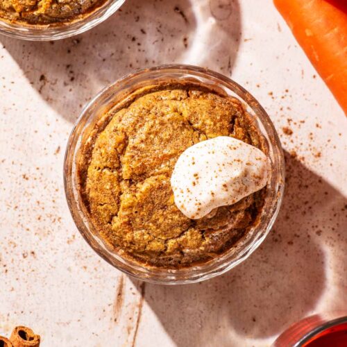 Orange-hued baked oats in small glass ramekins, topped with yogurt.