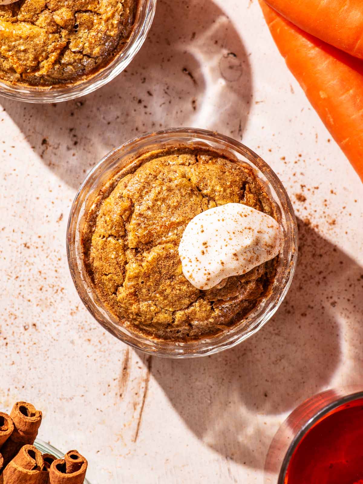 Orange-hued baked oats in small glass ramekins, topped with yogurt.