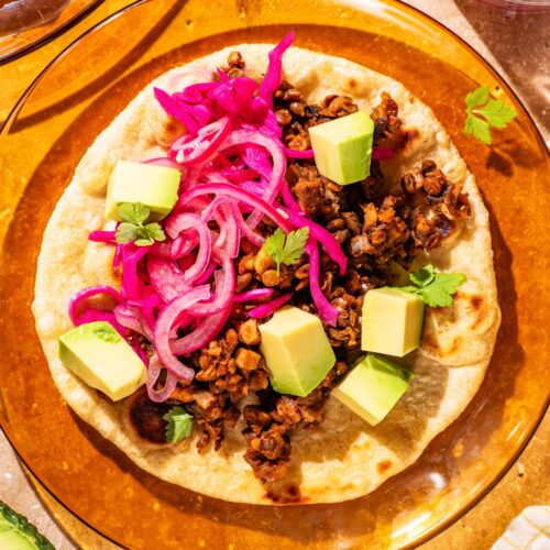 Lentil taco on a glass plate with avocado and pickled onion.