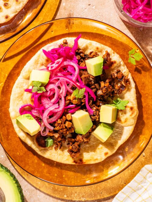 Lentil taco on a glass plate with avocado and pickled onion.
