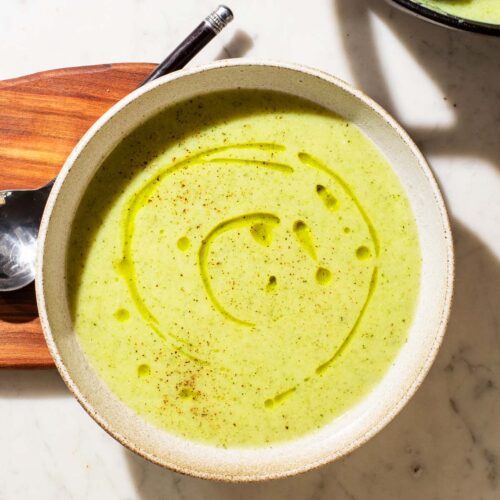 A bowl of light green soup on a wooden board with a spoon.