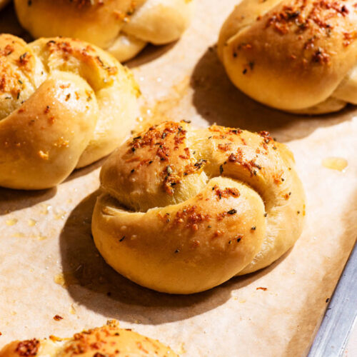 Knotted buns on a baking sheet, topped with garlic.