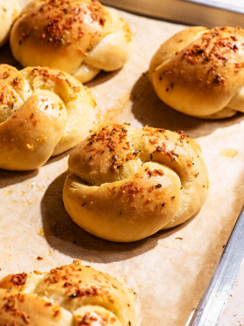 Knotted buns on a baking sheet, topped with garlic.