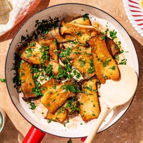 Seared king oyster mushrooms in a frying pan with chopped parsley.