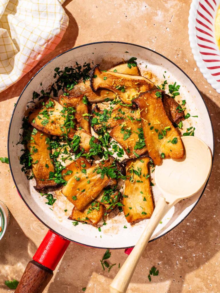 Seared king oyster mushrooms in a frying pan with chopped parsley.